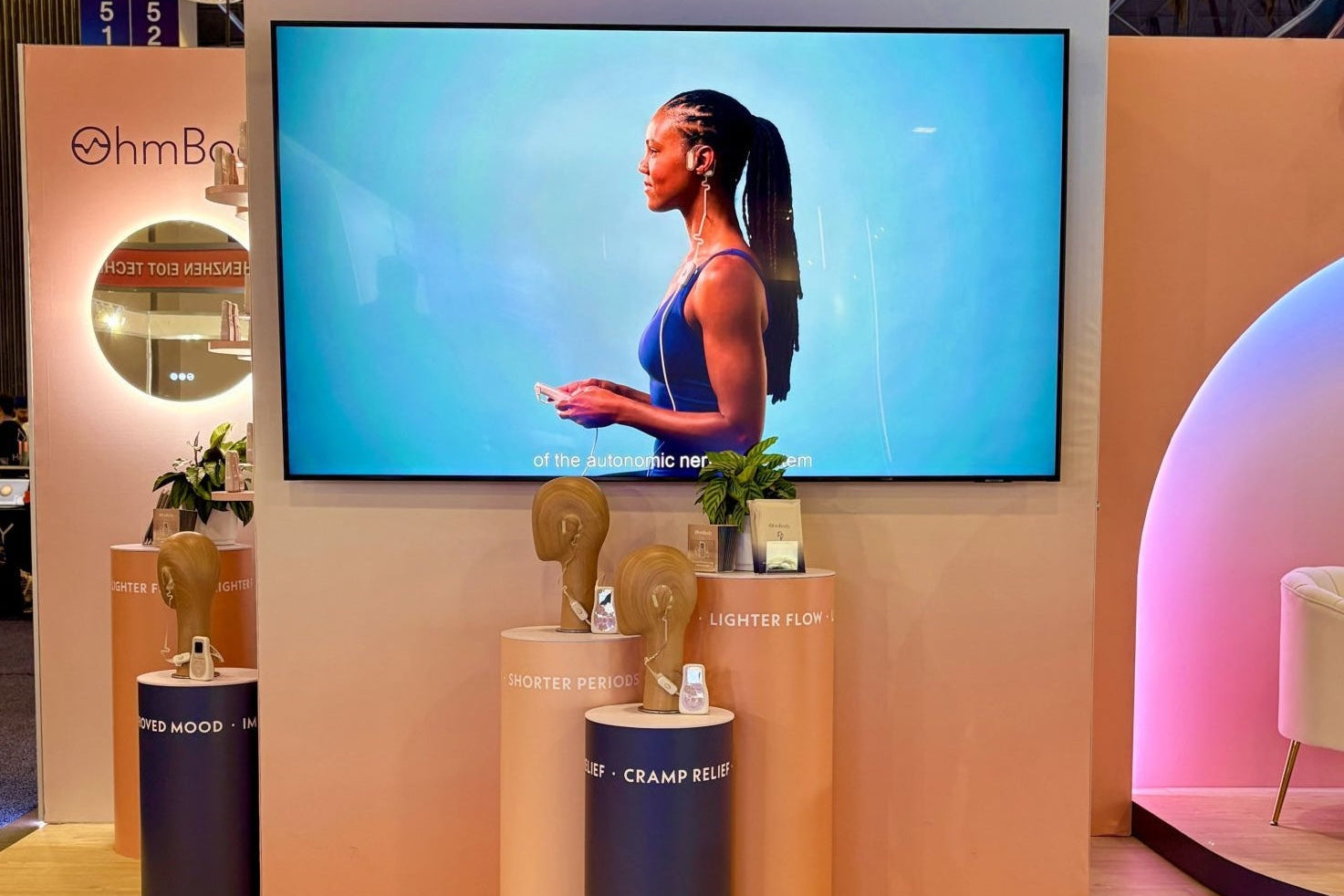 OhmBody booth at CES with pale pink walls and tv screen