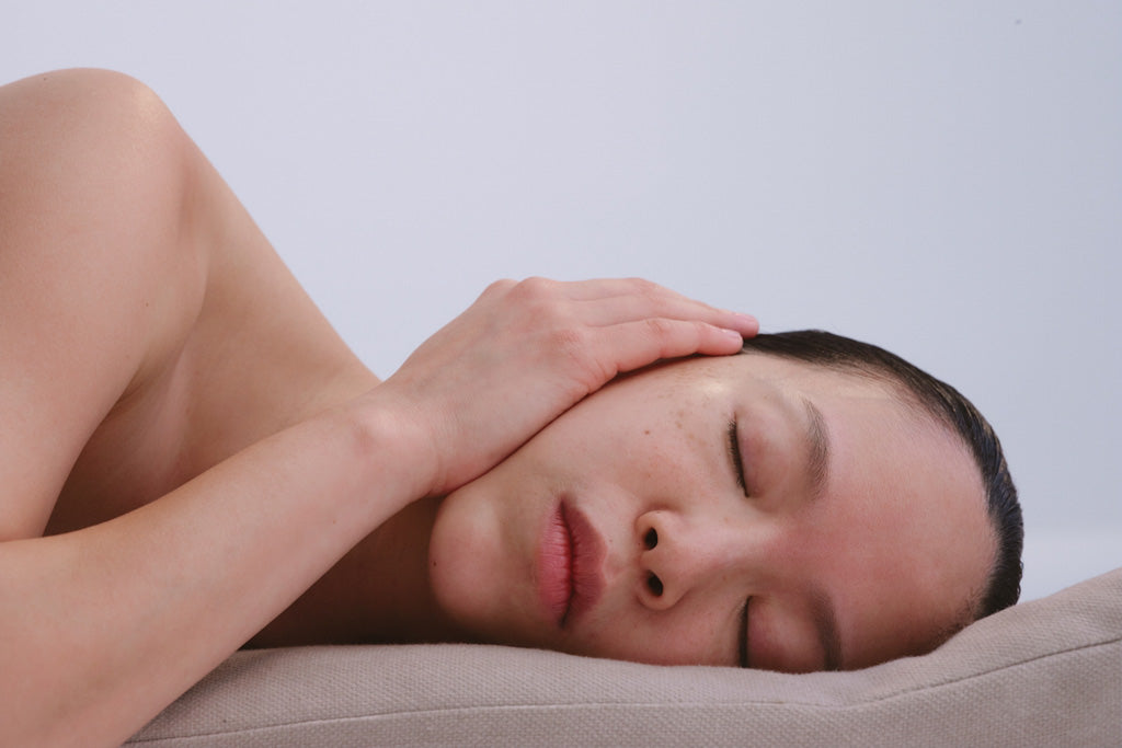 women holding her outer ear while laying on soft surface